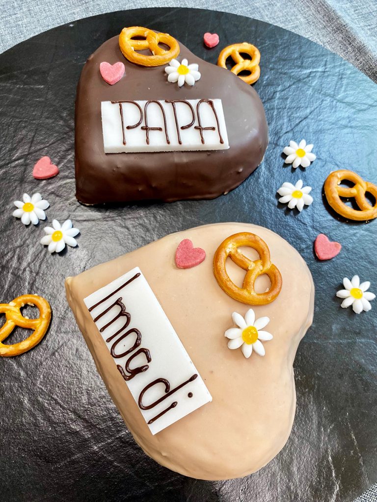 Zwei Herzen hell/dunkel mit Herzen, Blumen, Salzbrezel dekoriert und den Schriftzügen "Papa" und "I mog di"
